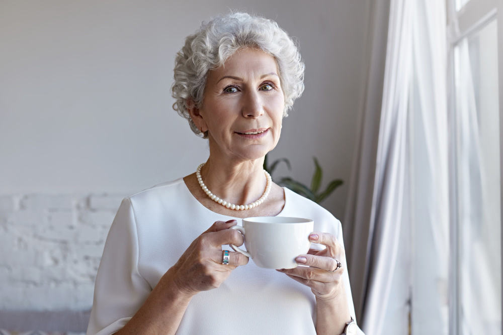Възрастна жена, която държи чаша с чай от билки
